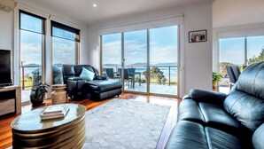 Amplia sala de estar con un sofá grande, una mesa de centro y una televisión. La habitación tiene ventanas grandes que ofrecen vistas al exterior.