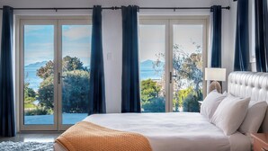 Un dormitorio con una cama grande, vistas al mar y una ventana con cortinas.