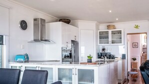 Una cocina moderna con armarios blancos, una campana extractora de acero inoxidable y un horno empotrado. Hay una zona de comedor con una mesa de madera y sillas negras.