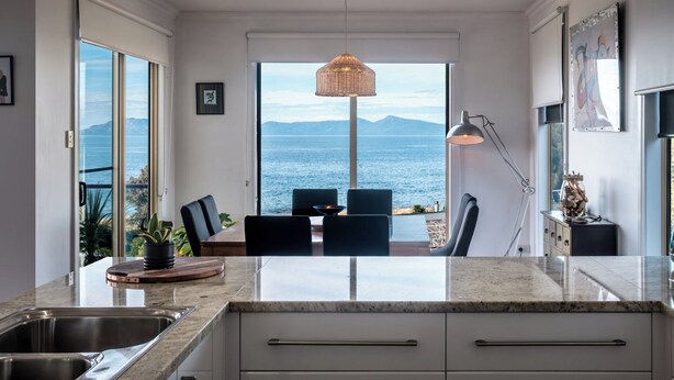 Una cocina moderna con una isla grande, un comedor con sillas y vista al mar.