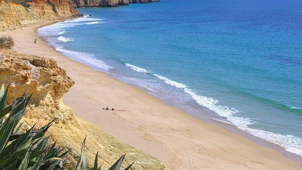 A coastal beach with clear blue waters, sandy shore, and rocky cliffs.