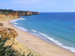 A beach with clear blue water, sandy shore, and rocky cliffs.