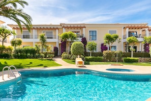 A swimming pool with a geometric tile pattern, surrounded by a well-maintained lawn and various shrubs.