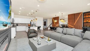 Una sala de estar moderna con un sofá gris, una mesa de centro y una pantalla de televisión mostrando una escena tropical.