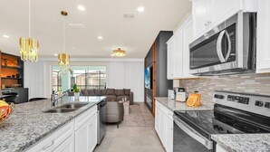 Una cocina moderna con encimeras de granito, electrodomésticos de acero inoxidable y un comedor con sofá gris e iluminación de araña.