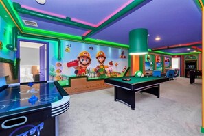 A brightly lit room with a pool table, a foosball table, and a mural featuring Mario and Luigi.