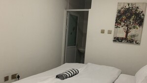 Ein ordentlich bezogenes Bett mit weißen Leinen und einem gestreiften Handtuch, ein Baumgemälde an der Wand und eine Tür zu einem Badezimmer.
