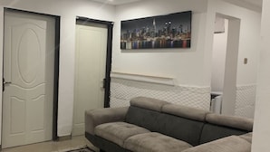 Ein modernes Wohnzimmer mit einem Ecksofa, einem gemusterten Teppich und einem Stadtbild an der Wand.