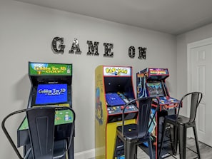 Trois bornes d’arcade, une chaise et une enseigne murale sur laquelle on peut lire « GAME ON ».