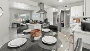 A modern kitchen with white cabinets, a central island, and a dining area with a glass table and black placemats.