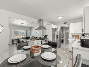 A modern kitchen with white cabinets, a central island, and a dining area with a glass table and black placemats.