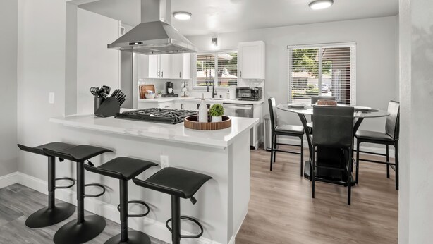 A modern kitchen with white cabinets, a central island with stools, and a dining area with a round table and chairs.