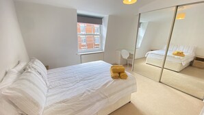 Une chambre moderne avec un grand lit, un miroir et une vue sur un immeuble en briques.