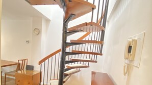 Un escalier en colimaçon avec des marches en bois et des rampes noires, une table à manger en bois avec des chaises, et un banc en bois.