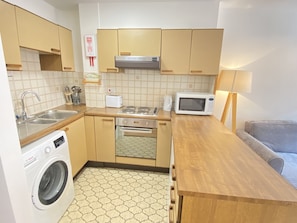 Compact kitchen with a Bosch washing machine, microwave, and toaster, featuring an oven and hexagonal tile flooring.