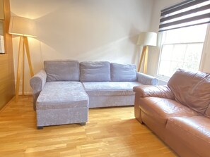 Relax in this inviting living room with a sofa and leather couch, surrounded by natural light and comfortable seating.