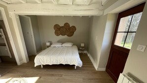 Ein Schlafzimmer mit einem großen Bett, Holzboden, einer Wandleuchte und einem Fenster mit Blick auf Bäume.