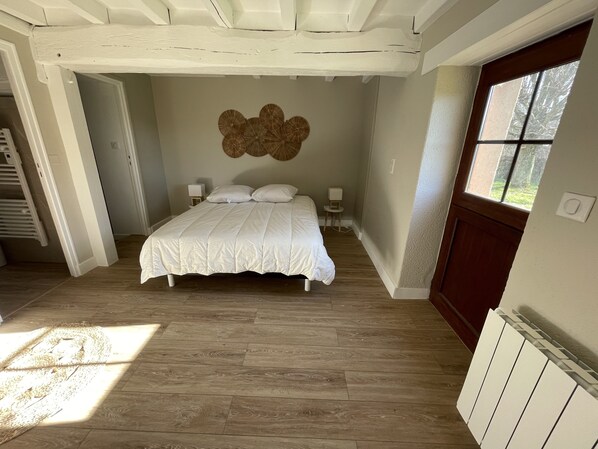 Una camera da letto con un letto grande, pavimento in legno, lampada a parete e finestra con vista sugli alberi.