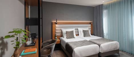 Ein Hotelzimmer mit einem Doppelbett, Nachttischen, einem Schreibtisch mit Stuhl, einer Zimmerpflanze und einem großen Fenster mit Vorhängen.