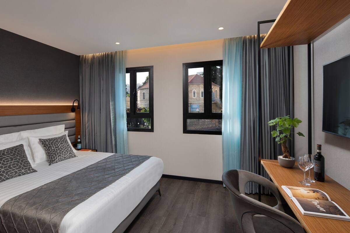 A modern hotel room with a large bed, a desk with a chair, a TV, and a window with curtains.