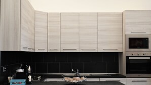 A modern kitchen with light wood cabinets, a black backsplash, and stainless steel appliances including a microwave and oven. - Gikla maison in the heart of Catania (Catania)