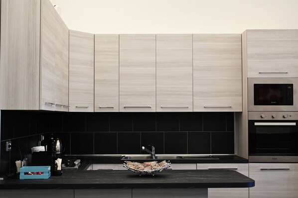A modern kitchen with light wood cabinets, a black backsplash, and stainless steel appliances including a microwave and oven.