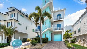 A modern multi-story residential building with a blue and white color scheme, a central staircase, and a driveway leading to a garage.