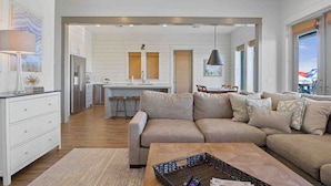 Una sala de estar moderna con un sofá color beige, una mesa de centro y una cocina al fondo.
