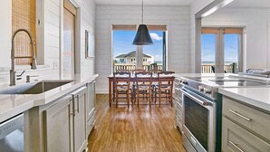 Una cocina moderna con piso de madera, electrodomésticos de acero inoxidable y un comedor con vista al mar.