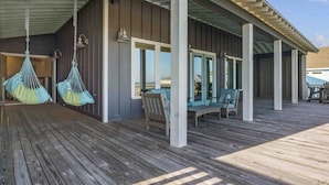 Un espacio al aire libre techado con cubierta de madera, con hamacas colgando y una zona de estar con sillas y una mesa.