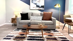 A modern living room with a grey sofa, patterned cushions, a round coffee table, and a geometric rug.