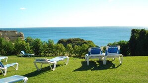 A grassy area with lounge chairs facing a coastal view. - Vilas Marrocha (Lagoa)