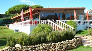 A building with a white exterior, a red roof, and a balcony with red umbrellas. - Vilas Marrocha (Lagoa)