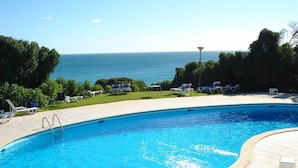 A swimming pool with a view of the sea, surrounded by lounge chairs and greenery. - Vilas Marrocha (Lagoa)