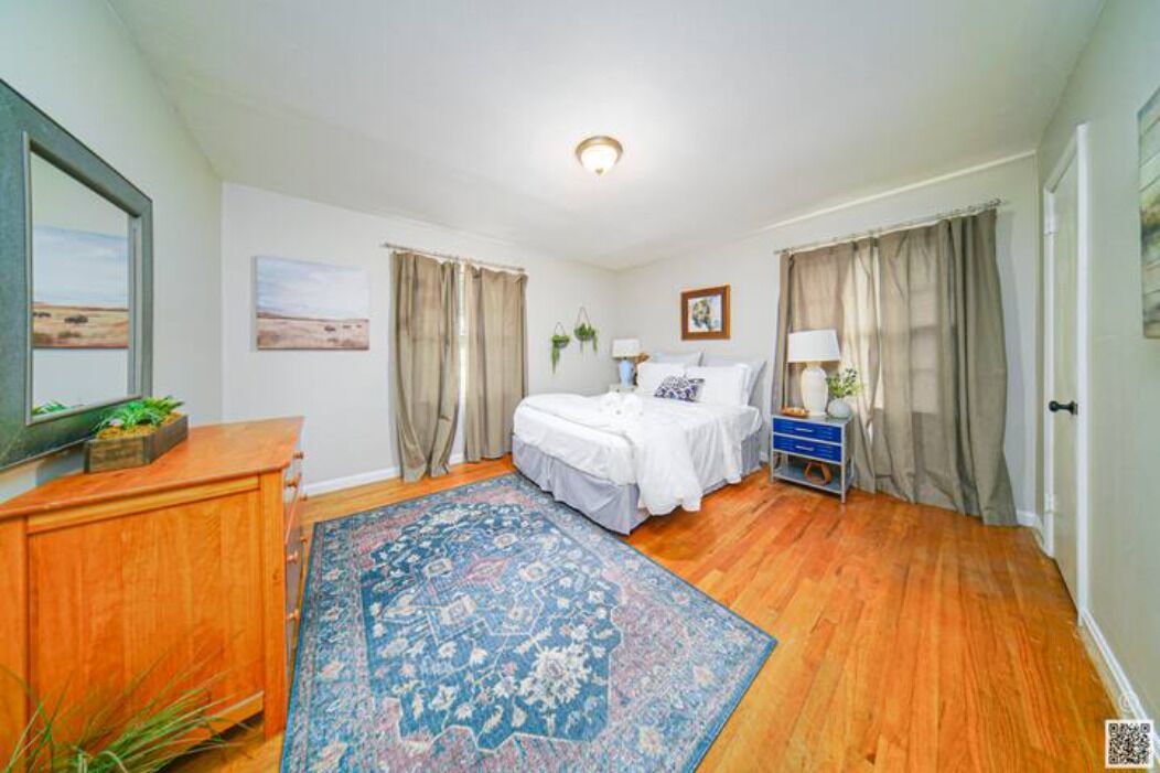 A bedroom with a bed, a dresser, a nightstand, a lamp, and a large rug.
