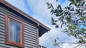 A house with a grey exterior, wooden window frames, a wooden deck, and a view of a green landscape with mountains in the background. - Tiny House Garden - Praia Grande - SC (Praia Grande)