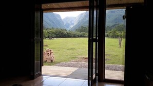 A room with a large glass door leading to a grassy outdoor area with mountains in the background. - Tiny House Garden - Praia Grande - SC (Praia Grande)