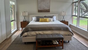 A bedroom with a bed, bedside tables, a bench, and large windows. - Inks Lake Open Water and Pet friendly home (Burnet)