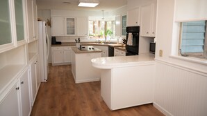 A modern kitchen with white cabinetry, a central island, and a built-in oven. - Inks Lake Open Water and Pet friendly home (Burnet)