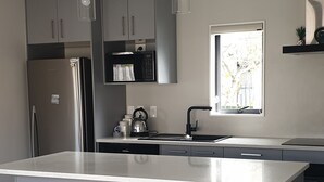 Una cocina moderna con una isla central, taburetes de bar, electrodomésticos de acero inoxidable e iluminación colgante.