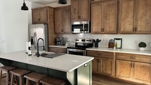 Eine moderne Küche mit Holzausstattung, Edelstahlgeräten und einer großen Kochinsel mit Barhocker.