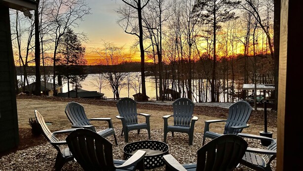 Eine Terrasse mit Adirondack-Stühlen, die auf einen See bei Sonnenuntergang blicken.