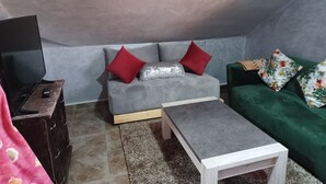 A small, cozy room with a grey sofa, a green sofa, a wooden coffee table, and a TV on a wooden stand. - Belle Vue Studios & Apartments (Ifrane)