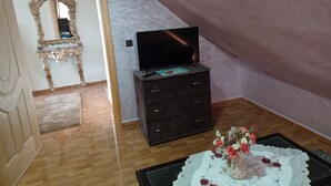 A room with a wooden floor, a dark wooden dresser with a flat-screen TV on top, a decorative vase with flowers, and a large ornate mirror on the wall. - Belle Vue Studios & Apartments (Ifrane)