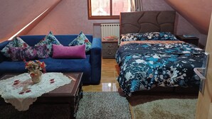 A cozy attic bedroom with a sloped ceiling, a bed with a floral duvet, a blue sofa with patterned cushions, and a small table with a vase. - Belle Vue Studios & Apartments (Ifrane)