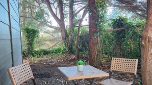 An outdoor seating area with two wicker chairs and a small table, surrounded by trees and a gravel ground. - Modern Retro Retreat (McKinleyville)