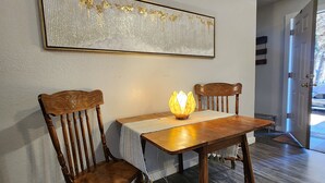 A dining area with a wooden table and chairs, a decorative wall hanging, and a door leading outside. - Modern Retro Retreat (McKinleyville)