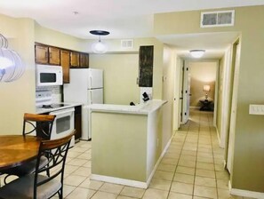 Kitchen area with central island, microwave, and refrigerator, adjacent to a dining table and hallway.