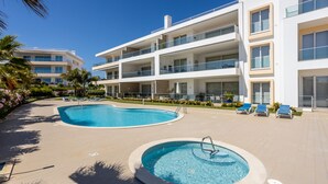 Un hotel moderno con zona de piscina, que incluye una piscina rectangular grande y un jacuzzi más pequeño.
