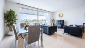 Una sala moderna con una mesa de vidrio, dos sofás, un televisor y un amplio ventanal con vistas a edificios.
